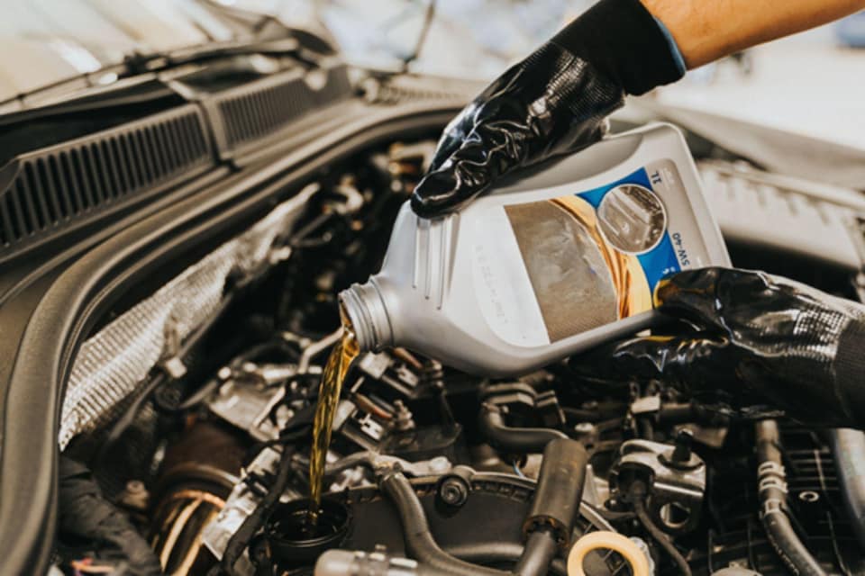Car mechanic pouring engine oil in a car 