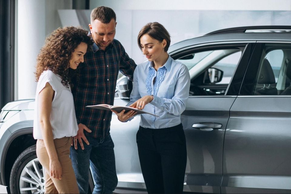 young couple talking to sales person in a car showroom