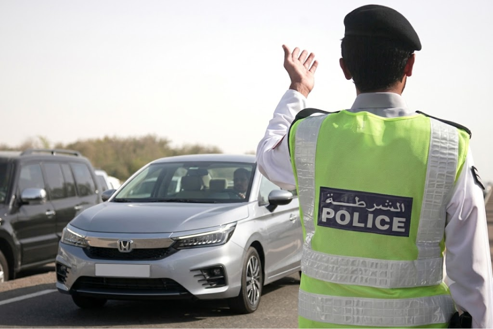 A traffic police officer in a high-visibility vest gesturing next to a silver Honda City