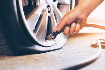 Close-up of a person inflating a flat car tire using an air hose.