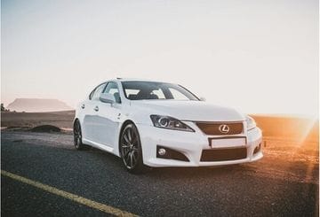 A white Lexus sedan parked on an open road with a dramatic sunset and clear sky.