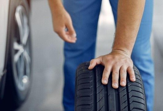 Person inspecting a car tire, checking tread depth and condition.