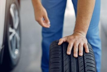 Person inspecting a car tire, checking tread depth and condition.