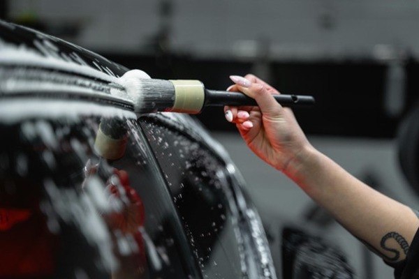 A Hand cleaning car exterior with brush and foam.