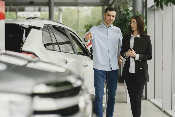 A sales representative and customer stand beside a white Toyota RAV4 in a modern showroom, 