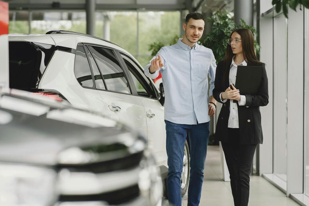 A sales representative and customer stand beside a white Toyota RAV4 in a modern showroom, 