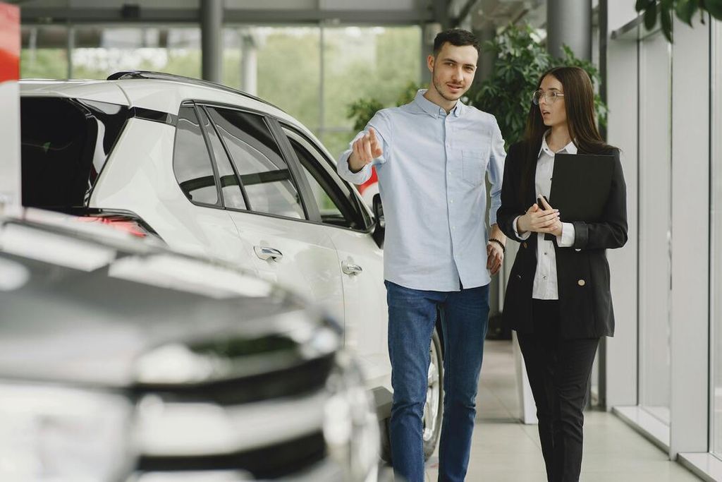 A sales representative and customer stand beside a white Toyota RAV4 in a modern showroom, 