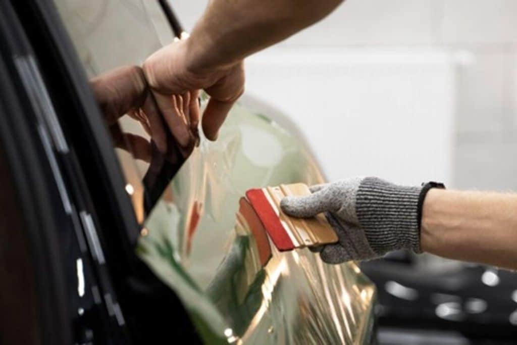 A person is applying a protective film wrap to a car's exterior.