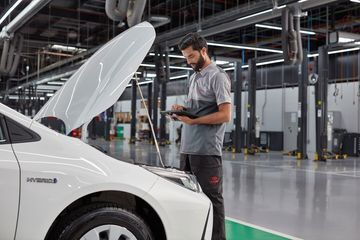 Mechanic inspecting a Toyota car inside a well-lit automotive service center.