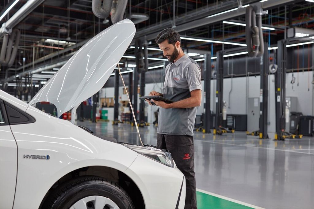 Mechanic inspecting a Toyota car inside a well-lit automotive service center.