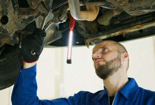 Mechanic inspecting car undercarriage with a wrench and work light.