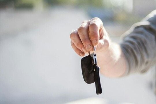  A hand handing over car keys, signifying a change in ownership.