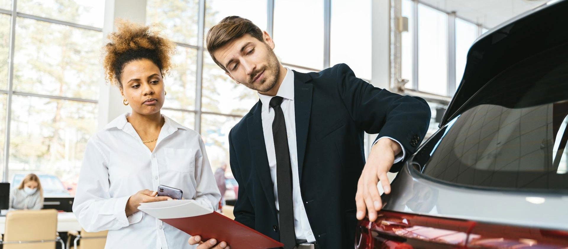 Car salesperson showing rear of vehicle to a customer inside a dealership.