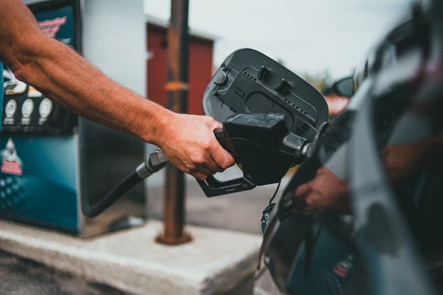 A hand holding a nozzle while refueling a car at a fuel station.